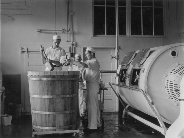 Several men in white are shown churning a one-ton tub of butter for exhibit at the State Fair.