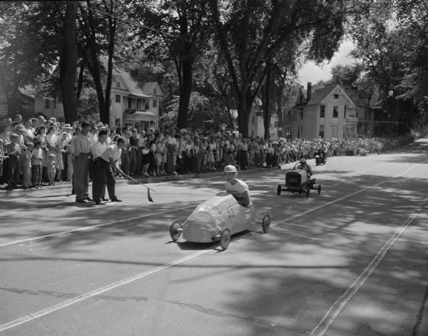 Crowd and officials watch Soap Box Derby contestants at the finish line on East Gorham Street.