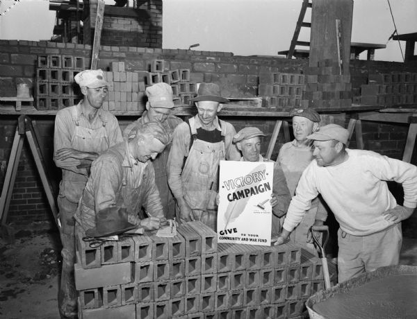 Madison Building and Construction Trades workers on the job at the Hoofer Glass Co. take time out to sign their pledge cards for one day's pay to the Madison War Chest. Pictured left to right, first row are: J.M. Lendborg, Alex Wicklender, and Elnar Strand. In the top row from left to right are: Robert Hildebrandt, Vincent Hildebrandt, John Porter, Elmer Waldo and Russell Hicks.