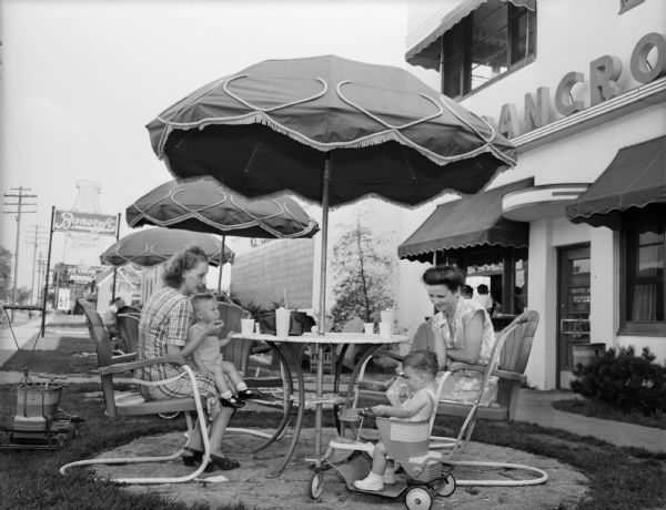 Bancroft Dairy "sidewalk fountain," 1010 South Park Street. Ruby Davenport and Dorothy Drifke are seated at an outdoor table. The table is covered by an umbrella and Ruby is holding her son Paul. Dorothy 's son Jim is in a stroller. "This is the first summer since the close of the war that we have been able to serve on the lawn," explained A.J. Sticha, manager, who says scarcity of ice cream resulted in this Bancroft Dairy service being abandoned during the war years.