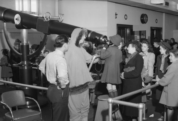 A line of people waiting to look through a large telescope at Manchester's Department Store at Christmas.
