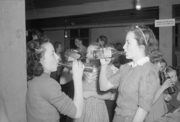 Three girls at the recreational center for school pupils at the Cottage Grove Town Hall drink from Nehi soda bottles.