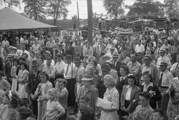 War workers, families and friends of Gisholt Machine Company at the company picnic held at the Blooming Grove Firemen's Park on Monona Drive. There is a carnival ride in the background. Shown are a group waiting for the crowning of the "Queen of Gisholt," Betty Cull, drill press operator at the plant.