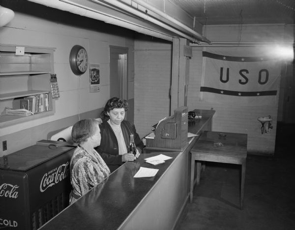 Two African American women at a counter in the USO Service Club. There is a Coca-Cola machine behind a counter. Probably taken in First Unitarian Society Parish Hall, 15 E. Dayton Street.
