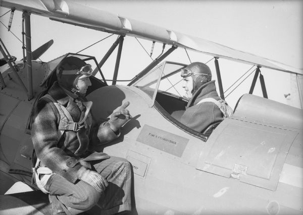 Instructor on the wing of a biplane talking with an airman trainee in the cockpit of a plane during flight training at Truax Field during World War II.
