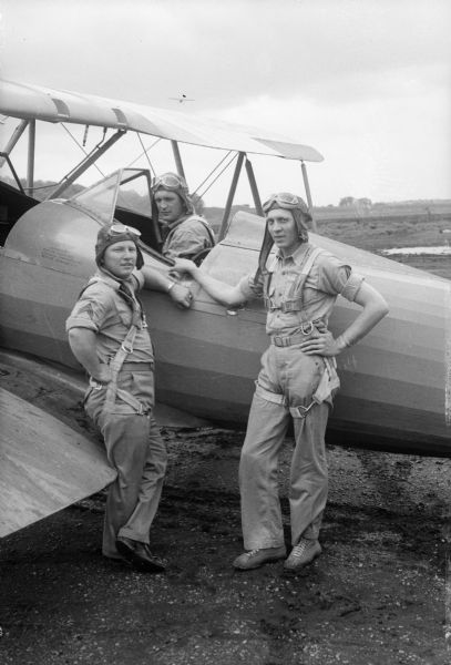 Airman trainee in cockpit of biplane with two flight instructors standing next to the plane at Truax Field during World War II.