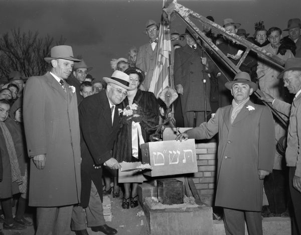 Ceremony for laying the cornerstone of the Beth Israel temple. Included in the crowd watching the ceremony are (left to right): A.J. Rosenburg, chairman of the board of directors, Emanuel Simon, Mrs. Meril Stein, A.J. Sweet, vice president, and Gus Widen of Vogel Brothers Construction.