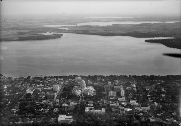 Aerial view of the city with horizon in the far distance. Includes the Wisconsin State Capitol, businesses, Lake Monona, and the surrounding neighborhoods.