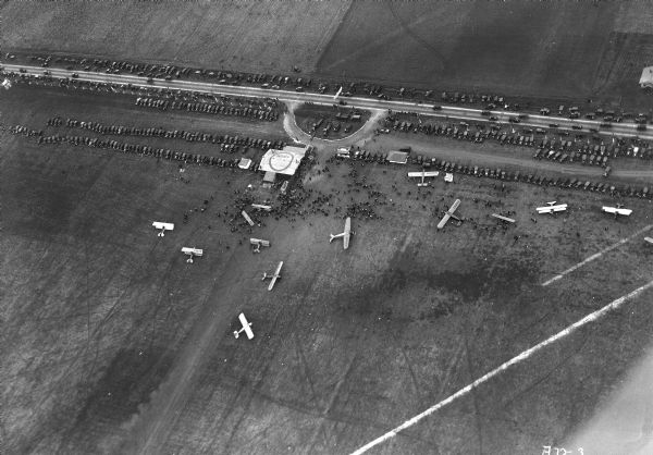 Aerial view of the Janesville airport during air races including airplanes in the air, the landing field, and airport structures.