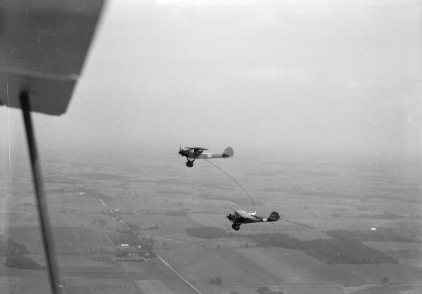 Two airplanes refueling in flight over Morey Airport.  The airport and farmland can be seen in the distance.