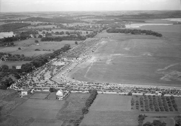 Aerial view of Pennco Field (Royal Airport), and Lake Monona near the city limits.  A crowd is gathered at the airport to watch an air show.