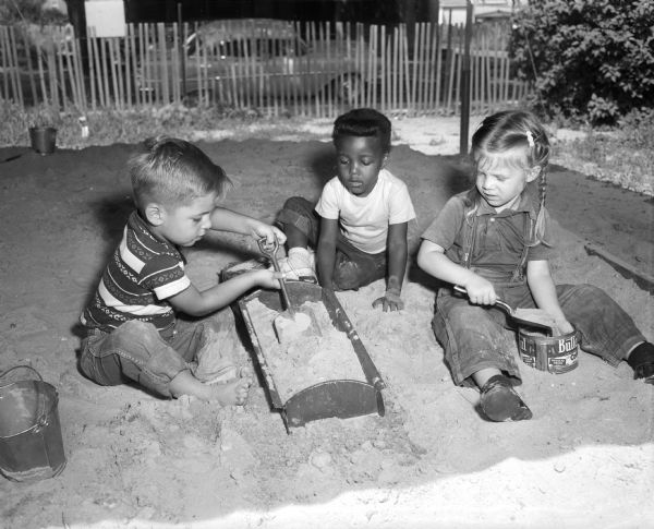 Three children, Jackie LeTourneau, Debra Ranes, and Ester Thayer, playing in the tot lot at the Neighborhood House, 768 West Washington Avenue.