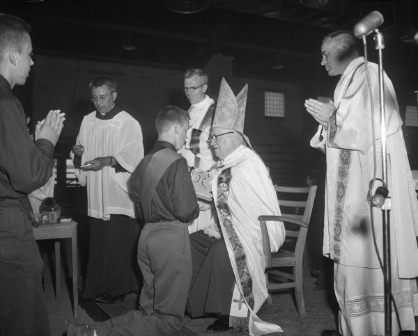 A boy scout receiving the Ad Altare Dei medal, the Catholic Church's award to boy scouts, from Bishop William P. O'Connor. Another boy scout and three other clergy observe the ceremony.