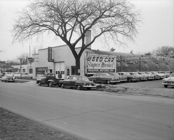 Exterior of the Madison Motors, Inc. Used Car Super Market, located at 1234 East Washington Avenue.  Other businesses include the Clifford Motor Bilsie Diamond Truck Sales, at 1208 East Washington Avenue, and the United Real Estate, United Sales Corp. auctioneers, at 1212-1214 East Washington Avenue.