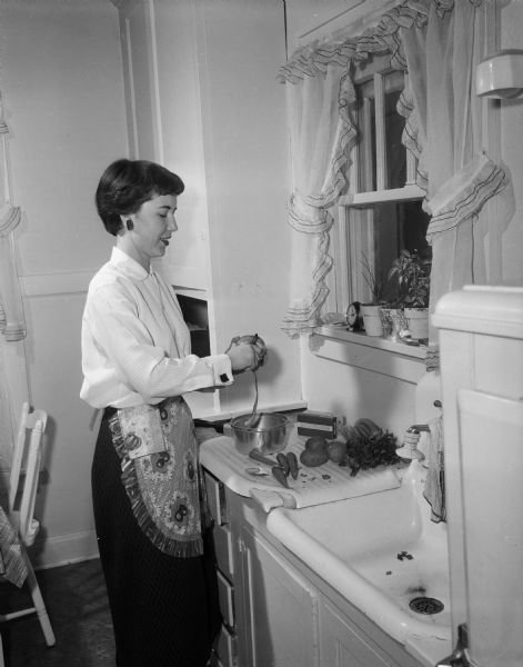 Joan McKerley peeling potatoes in the kitchen of a house she is sharing with three other young women at 2253 Rugby Row.
