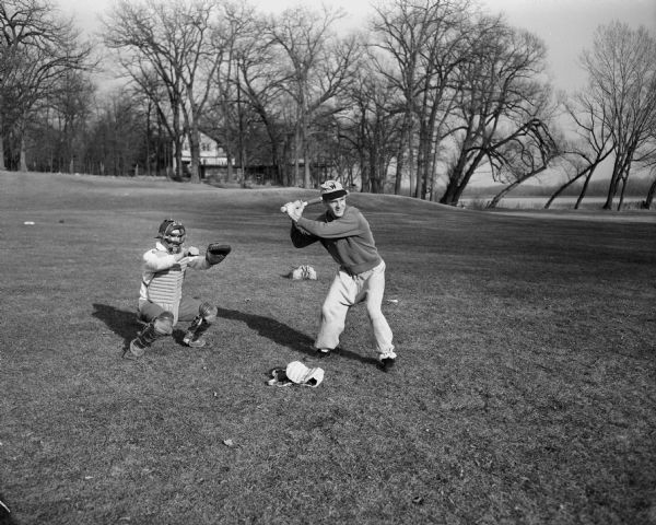 Don Woody, catcher, and Dave Baskerville, batter, members of the West High School baseball team. There is a lake in the background.