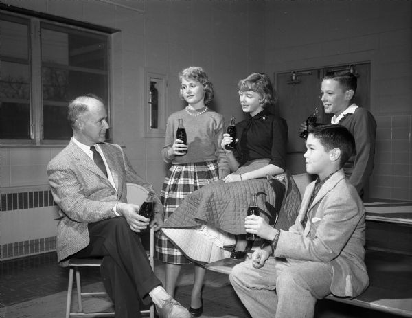 Four students, Kris Roisum, Karen Nelson, Charles Leveque, and Rick Radder, drinking sodas and chatting with Principal Emery Bainbridge at a Cherokee Heights School dance.