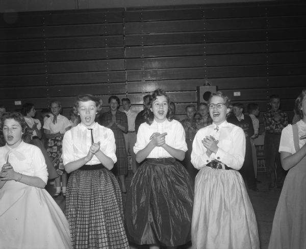 Students singing and clapping while doing the Hokey-Pokey at the Cherokee Heights School dance. In the foreground are Linda Billington, Ann Herreid, Merry Bliss, and another unidentified student.