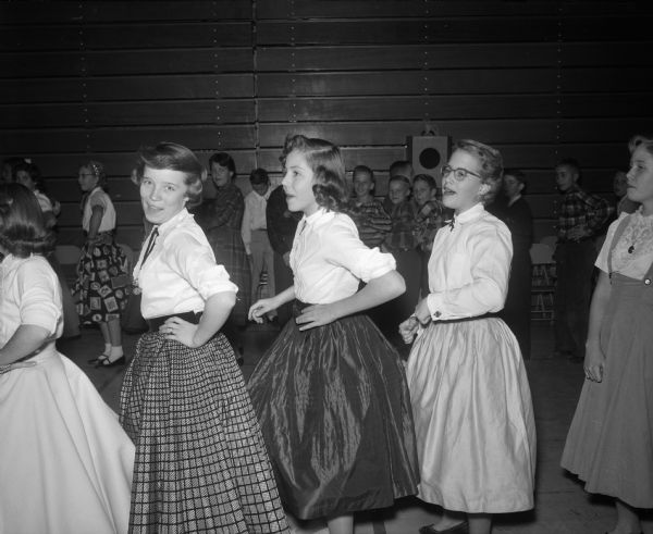 Students dancing in a circle doing the Hokey-Pokey at the Cherokee Heights School dance. In the foreground are Linda Billington, Ann Herreid, Merry Bliss, and another unidentified student.