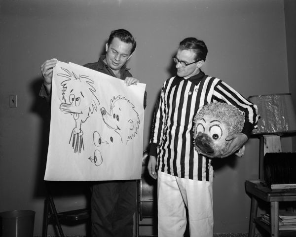 Walt Kelly, famous cartoonist, holds up two versions of his Pogo character to a Pogo impersonator.