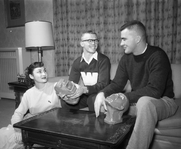 University of Wisconsin students Pamela Lynch, Homecomming publicity chairman, Richard Hammes, Homecoming Chairman, and Jack Heffernan, Chairman of the Pep Rally, admire the "Yell Like Hell" ceramic trophies which were awarded this year as a new feature of the traditional pre-game pep rally at the Memorial Union.