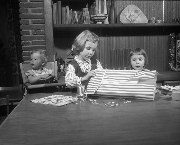 The children of Mr. and Mrs. Donald J. Reppen, 2801 Sylvan Avenue, wrapping a Christmas gift.  The children are, left to right: Sherri Lynn, 1; Karen, 5; and Nancy Jane, 3.