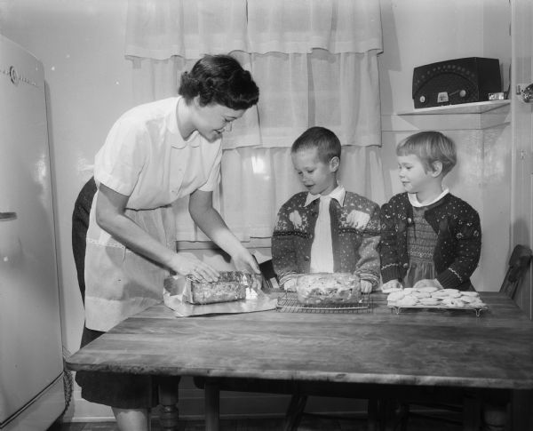 Joan Meyer, 701 Baltzell Street, wrapping loaves of Christmas bread. Watching are children Donnie Meyer, 5, and Mary Jane Meyer, 4.