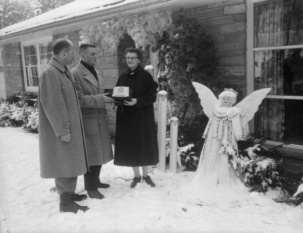 Ruth Bass, 4216 Mandrake Road, receiving a clock radio as a prize in the Christmas outdoor home lighting contest from Lucien G. Schlimgen, Jr., president of the Junior Chamber of Commerce, and Tom Towell, contest chairmen.
