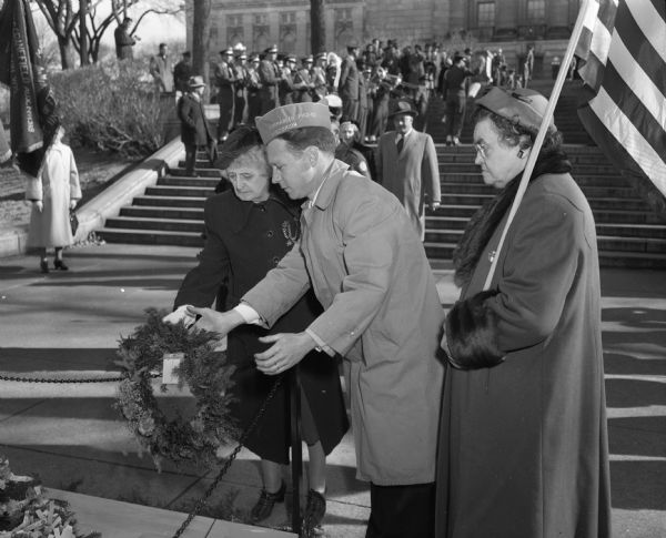Nena Aylward, left, of the Women's Relief Corps, is placing a wreath on the cenotaph in Armistice Day ceremonies in Capitol Park. Assisting is Clarence R. Starr, Madison Veterans of Foreign Wars commander, and Elsie Jensen of the women's Relief Corps color guard.