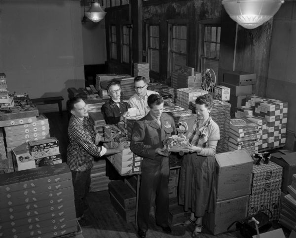 Empty Stocking Club workers, Sgt. Earl Nevin and Mrs. Alice Shores (holding a musical duck). Other workers behind them are Bill Doudna, Mrs. Lucille Knoche, and Lloyd Helm, looking over supplies of toys to be distributed at the Toy Depot opening Friday at the Community Center.