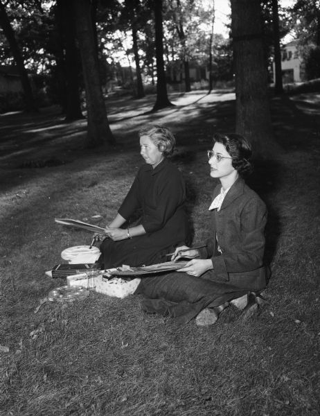 Ellsworth Mack and Charlotte Martin, members of the Shorewood League Painting and Sketching class, sitting outdoors in Shorewood Hills, painting an autumnal scene.
