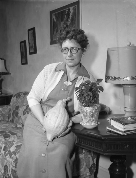 Mrs. Henry Hetland with a grapefruit plant that she grew from seeds, and a squash that grew from a vine she planted outside her home. She has observed that "plants are like people — in the things they need, the way they turn to the sun, and how they respond."