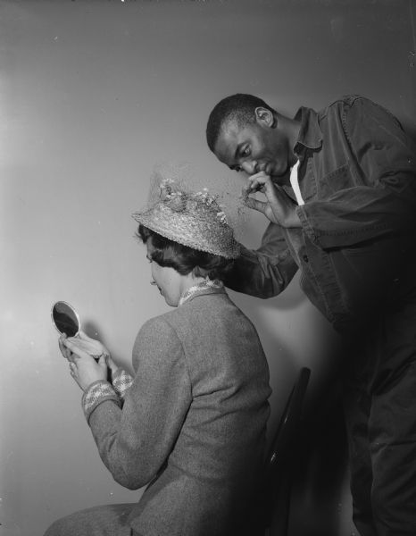 Dottie Hildebrandt, a Wauwautosa senior in Recreation at the University of Wisconsin, trying on spring hat, assisted by Lonnie Graham. The hat, titled "Gray Mist," was designed by Walter J. McLoughlin, who won third prize in an Easter bonnet designing contest for Veterans Administration Hospital non-ambulatory patients.
