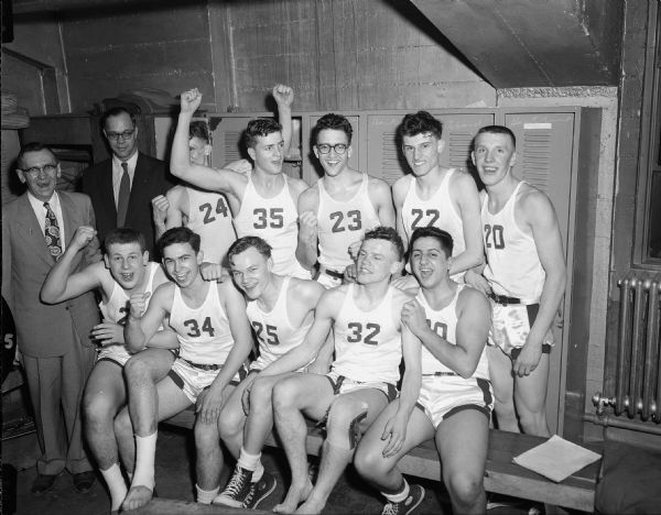 Group portrait of boys' high school basketball team, celebrating in the locker room with two coaches after a WIAA Basketball Tournament game.