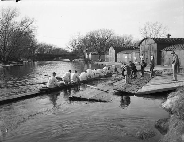 University of Wisconsin crew gets into their shell from the dock on the Yahara River with Trachte boat houses in the background. View looking northwest toward Johnson St. bridge.