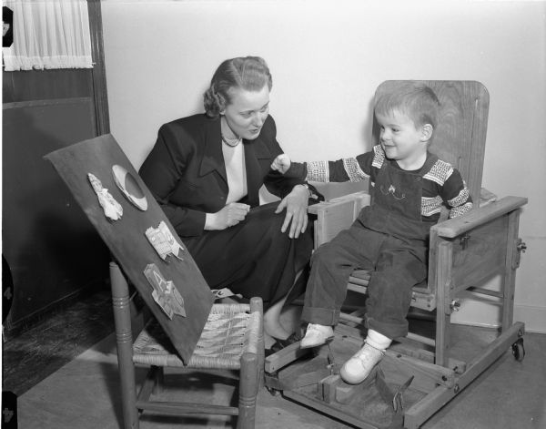 Joan Kain, speech therapist, helps Tommy Manning, age 3, who has cerebral palsy, learn to talk by showing him objects on a display board.  It is part of his treatment in the Easter Seal Cerebral Palsy Center at the University of Wisconsin Hospitals. He is the son of Mr. and Mrs. Roscoe Manning, Route 4, Richland Center, Wisconsin.