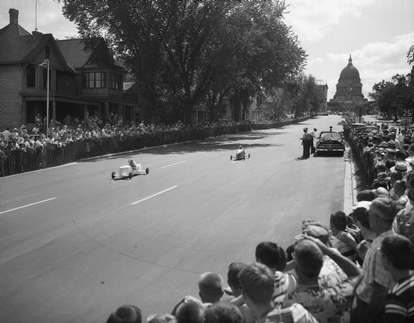 The Soap Box Derby held on East Washington Avenue leading from the Wisconsin State Capitol. Shown are two racers coming down the hill with the crowd along the course and the capitol building in the background.