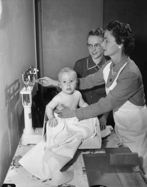 Members of Attic Angels Association volunteering at the Well Child Center, Wisconsin Neurological Foundation, 1954 East Washington Avenue. Included are Nancy Taborsky, 11-month old Ned Kessnich, and his mother, Mrs. Peter Kessnich.
