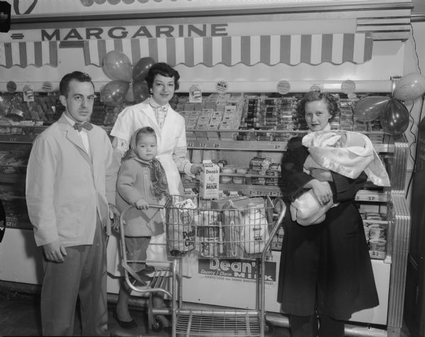 Two grocery store employees placing Dean's Milk in grocery cart for a woman and her two children.