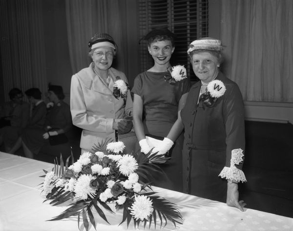 Mrs. Stanley Quinn, General Chairman of Dames Club Reception, with guests, Mrs. Blanche Stemm and Mrs. Rosa Fred, wife of University of Wisconsin President, Edwin Fred, standing at a table at the Dames Club reception at the Memorial Union.
