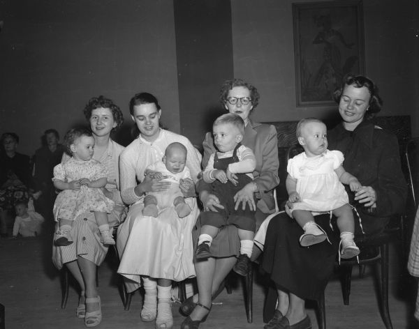 Four mothers sitting with their babies waiting to be "weighted in" at the American Legion Hall as contestants in the Legion baby show and child talent contest to be held on October 4th.