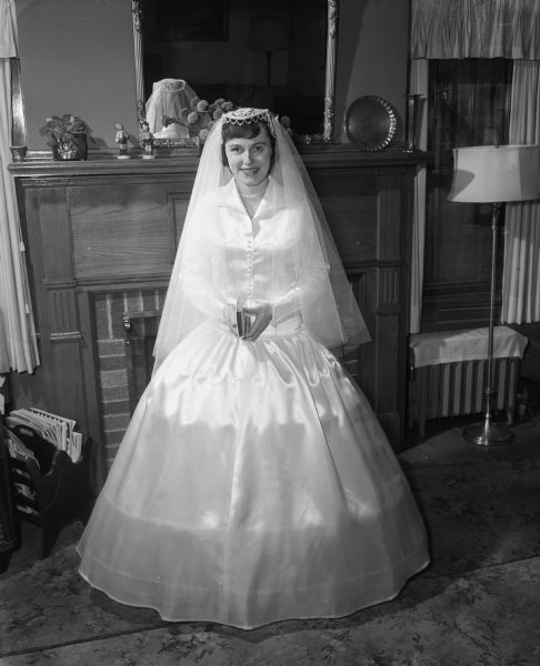 Portrait of Charlotte Dugan in wedding dress standing in front of a fireplace. She was a receptionist in the business office of Madison Newspapers, Inc. On January 29, 1955, she married Thomas E. Smith at St. Raphael Cathedral.