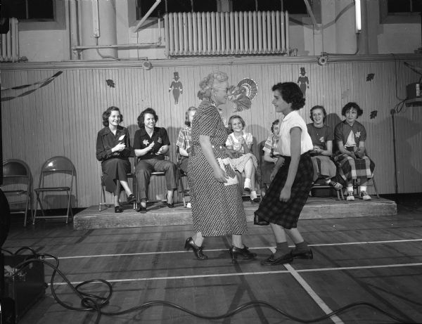Alma Stofen and Joanne Coyne dance to the accompaniment of clapping hands of women watching at a YWCA Health Education Department harvest square dance.