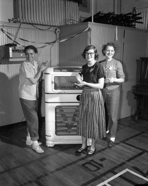 Audrey Lewis, health education director at the YWCA, Carol Radichel, and Mrs. Merrell Vertein standing around a jukebox at a YWCA square dance.