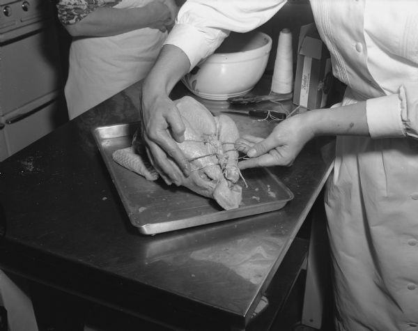 Close-up of a students' hands at a Vocational School cooking class sewing up a turkey after stuffing it with dressing. Another person is standing in the background.