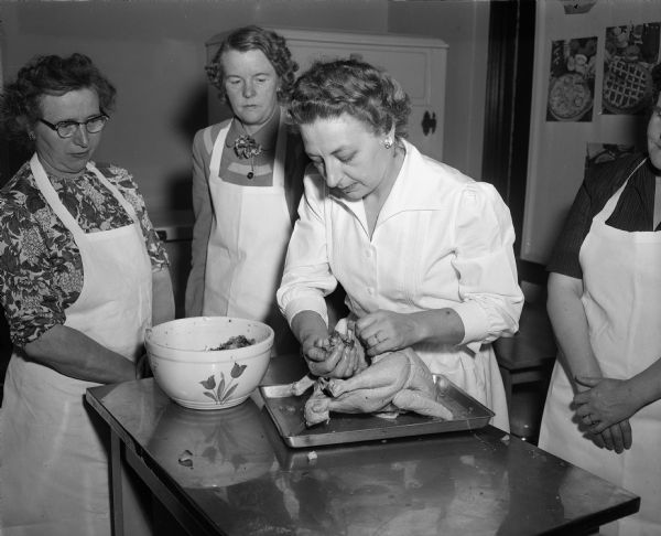 Mrs. Margot Nelson, the teacher, is showing students Bertha Haack and Josephine Scheerer the technique of stuffing the body cavity of a turkey at a Vocational School cooking class.