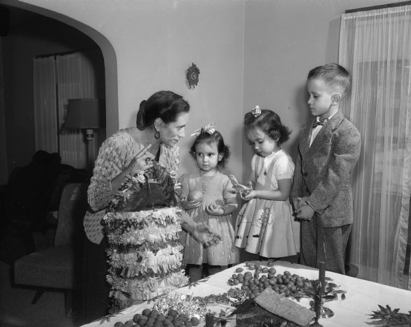 Mrs. Paul Meyer and children Freddy, Maria, and Elena, 2141 Keyes Avenue, filling a pinata for Maria's fouth birthday party and also Christmas.
