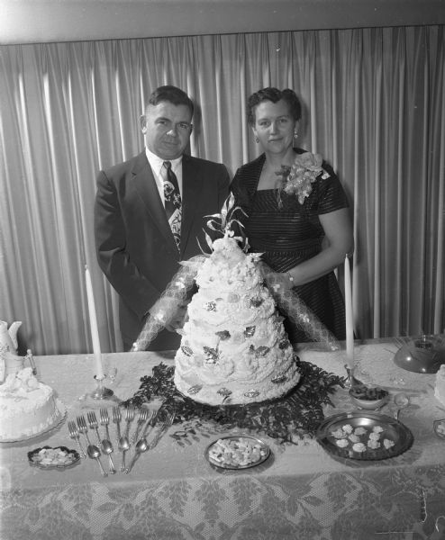 A couple posing with a cake at their silver wedding anniversary party.