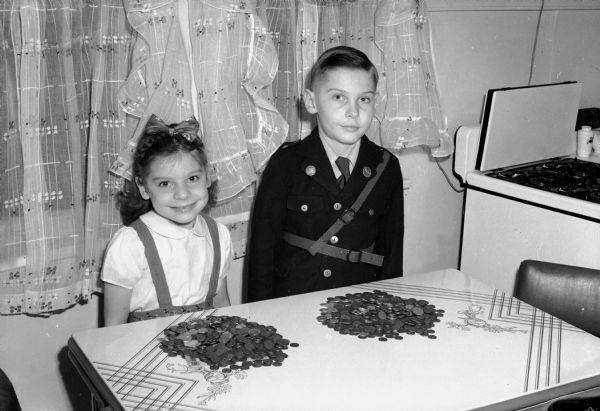Lorraine and Jackie Winters (ages 6 and 8 respectively), standing in front of piles of coins they have saved to buy a third War Bond. The children live at 1826 Spaight Street.