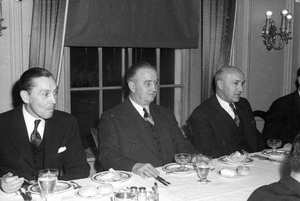 Three men seated at table at an East Side Business Men's Association dinner.